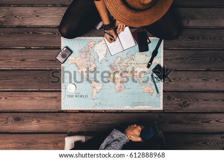 Man and woman planning vacation using a world map and other travel accessories. Woman noting the  discussion points in a small diary. Royalty-Free Stock Photo #612888968