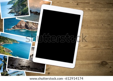 Vacation pictures on a wooden table and blank screen tablet. View from above.