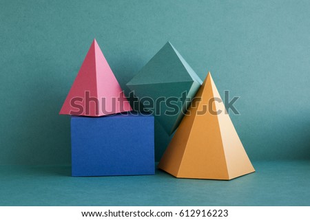 Colorful abstract geometric background with three-dimensional solid figures. Pyramid prism rectangular cube arranged on green paper. Yellow blue pink malachite colored geometrical shapes. Soft focus
