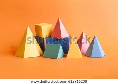 Colorful abstract geometrical composition. Three-dimensional prism pyramid rectangular cube objects on orange paper background. Yellow blue pink green colored solid figures, soft focus photo.