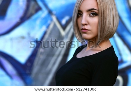 Portrait of an attractive and pretty young caucasian blonde girl with short hair on a background of a painted wall. A modern female portrait associated with street art and hooliganism