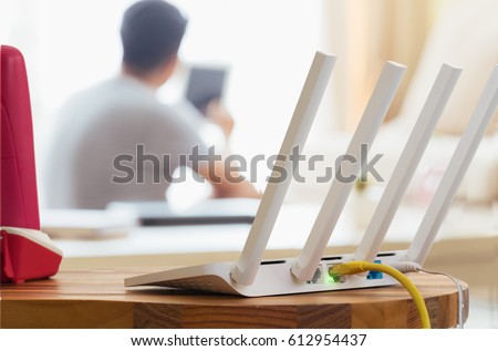 closeup of a wireless router and a man using smartphone on living room at home ofiice Royalty-Free Stock Photo #612954437