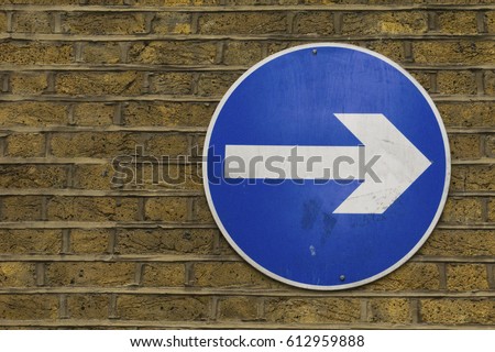Right pointing blue one way arrow sign on red brick wall
