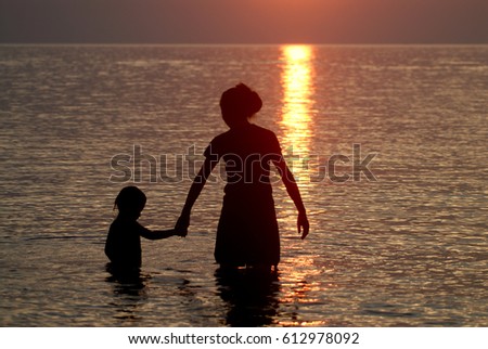 Mother and child holding hands in sunset at the beach.