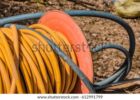 Yellow electrical cord wound around an orange metal spool with blurred background 