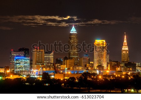 Brightly lit Cleveland Ohio under a full moon rising through a wisp of clouds