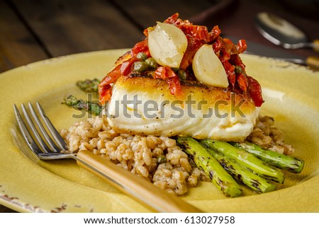 Dinner plate of fresh halibut fillet over bed farro with grilled asparagus, topped with salsa of red peppers, sundried tomatoes, garlic and capers on rustic yellow plate