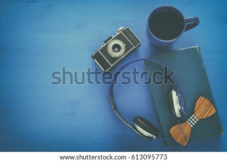 cup of coffee, old book, vintage photo camera and headphones on blue wooden background. top view image. Retro filtered