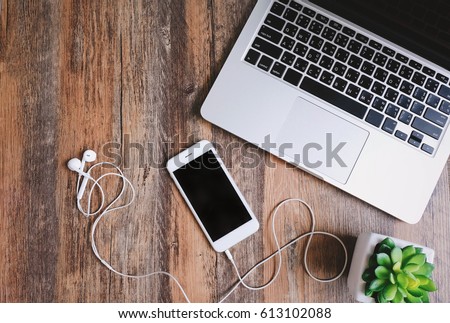 Flat lay photo of workspace desk with laptop, smartphone, earphones and green plant with copy space wooden background
