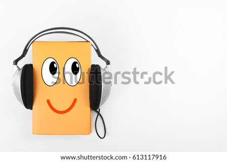 Audiobook on white background. Headphones put over yellow hardback book, empty cover, copy space for ad text. Distance education, e-learning concept