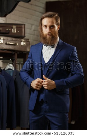 A young stylish man with a beard in a vintage cloth jacket. It is in the showroom, trying on clothes, posing. Advertising photo