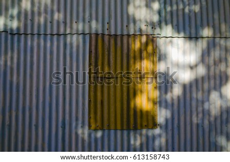 Dappled light from on corrugated iron barn wall on a sunny day. Grey corrugated metal wall with a brown section