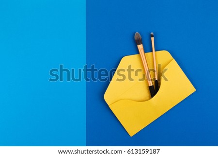Make up brushes in yellow open envelope on blue background. Top view. Flat lay. Copy space for text