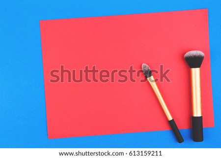 Make up brushes with red blank paper on blue background. Top view. Flat lay. Copy space for text