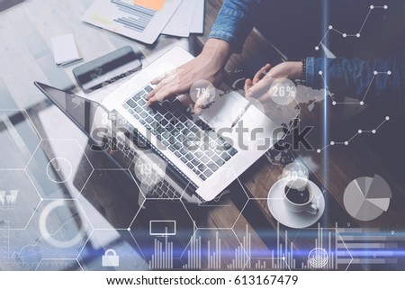 Businessman working at sunny office on laptop while sitting at the wooden table.Concept of digital screen,virtual connection icon,diagram,graph interfaces on background.Blurred,visual effects