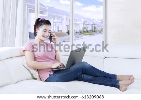 Picture of a pretty young woman sitting on the couch while working with laptop computer and mobile phone