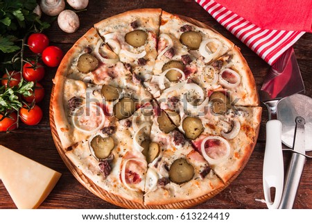 Italian hot pizza with mushrooms, onion, pickles, cheese and ham, sliced and served on wooden background with ingredients and special knife, flat lay. Restaurant menu photo.
