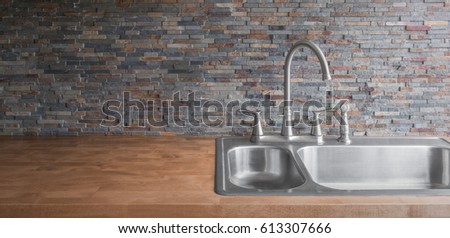 stainless steel sink and wooden kitchen counter and stone backsplash background Royalty-Free Stock Photo #613307666