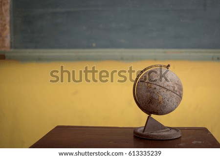 old orb or globe icon on student's table in front of classroom and chalkboard with teacher standing