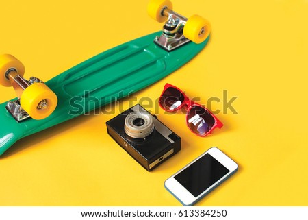 Fashion summer look concept. Green skateboard, red sunglasses, vintage camera and screen smartphone on a yellow background, top view. Trendy colorful photo. Flat lay