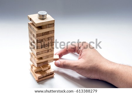 Remove the wood block from the base of wooden toy tower, that have coins on the top.
Show the meaning is "money unstable" Royalty-Free Stock Photo #613388279