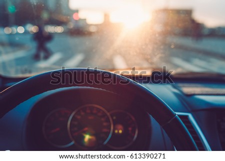 Closeup of the steering wheel in the car on the background of wonderful sunset. View of the road, pedestrian crossing. The view through car windscreen.  Warm toned picture, vintage tone.