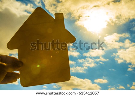 Man's hand holding a wooden toy house with window against blue sky. sun rays. sun light. eco bio building sweet home. house for rent