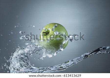Green apple and water splash on gray background.