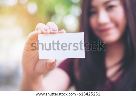 A beautiful woman holding and showing empty business card with smiley face in nature background