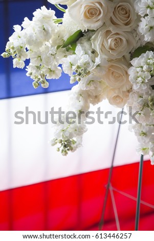 White flowers from a ceremonial wreath on a red, white, and blue background in honor and remembrance.
