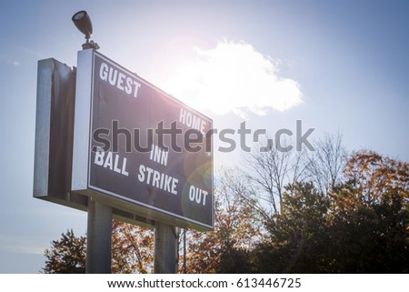 Close up of a scoreboard at a fenced in little league baseball field in the afternoon, with artificial sun flare added. 