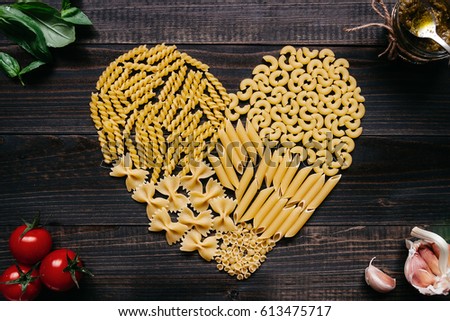 Dried pasta in heart shape top view. Pasta and vegetables on the dark wooden table.