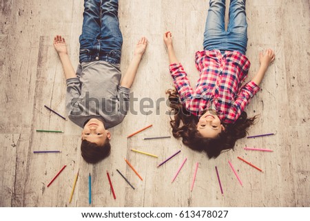 Top view of cute children looking at camera and smiling while lying on the floor at home
