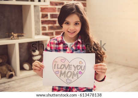 Cute little girl is showing her picture for mom and smiling while sitting on the floor at home