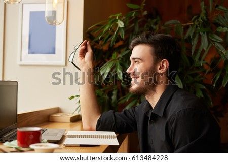 Side portrait of perfect look handsome caucasian man laughing and keep eye glasses in the hand. Guy get good news in the internet. Talented male editor start working morning in cafe