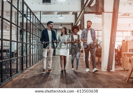 Catching up before meeting. Full length of young modern people in smart casual wear discussing business and smiling while walking through the office corridor Royalty-Free Stock Photo #613503638