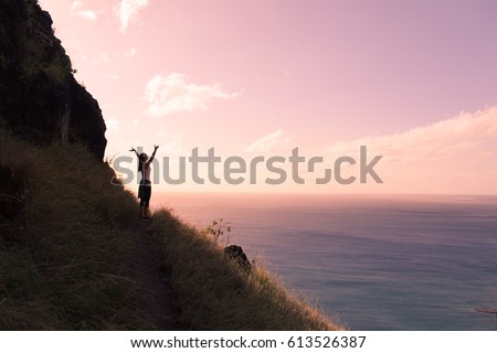 Active healthy lifestyle concept.  Happy female hiker standing on a cliff with her arms up in the air feeling free Royalty-Free Stock Photo #613526387