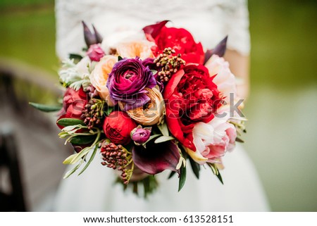 Beautiful red bouquet. The bride is holding a bouquet in her hands. Flowers of the bride on the background of a white dress.