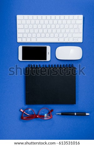 top view of keyboard, eyeglasses, smartphone and notebook on office table isolated on blue