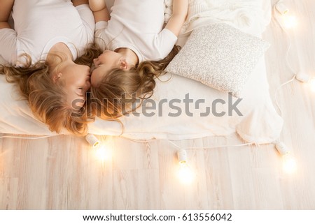 Mother and daughter lay on the bed and kiss. View from above. Togetherness. Loft interior. White