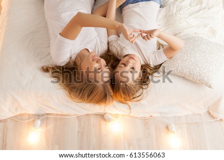 Mother and daughter lay on the bed and make heart by hands. View from above. Togetherness. Loft interior. White