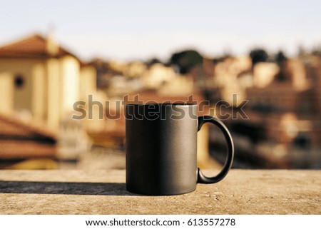 Black tea or coffee cup with copy space for the logo, text or design over blurred urban background. Mock up, drink concept. Hot coffee mug on a sunlight background. Blank tea mug on a concrete surface
