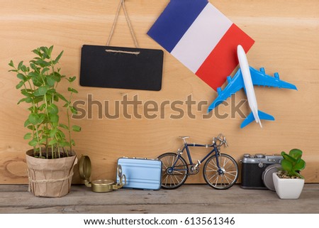 Travel time - blank blackboard, flag of the France, airplane model, little bicycle and suitcase, camera, compass on wooden background