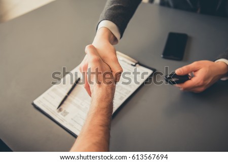 Visiting car dealership. Men are shaking hands while signing documents