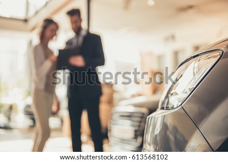 Beautiful young woman is talking to handsome bearded sales manager while choosing a car in dealership Royalty-Free Stock Photo #613568102