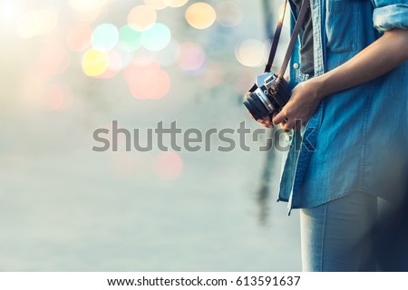 Close-up shot of young woman hand holding a retro film camera. Hipster girl photographer with beautiful blurred light bokeh. Vintage filtered color effect style.
