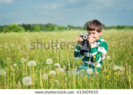 Child wathing in camera on the field with dandelions. Boy playing on the meadow in summer