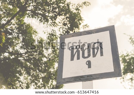 Wooden stop sign in Thai language with tree and cloudy sky for background