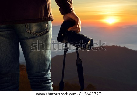 Hand of a man holding a camera on mountain and sun background