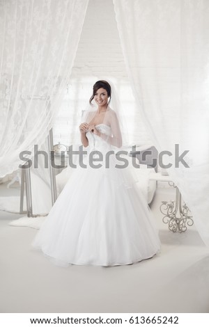 Beautiful bride standing in bedroom in wedding dress, smiling happy. Full size.